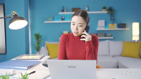 Mujer-Asiática-Llamando-Al-Teléfono-Y-Teniendo-Una-Conversación-Enojada-Mientras-Trabaja-Desde-Una-Computadora-Portátil